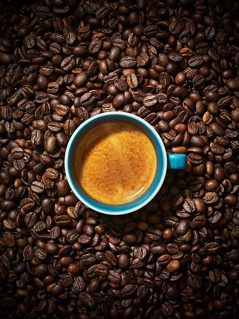 An espresso coffee in a blue ceramic mug against a coffee bean background.