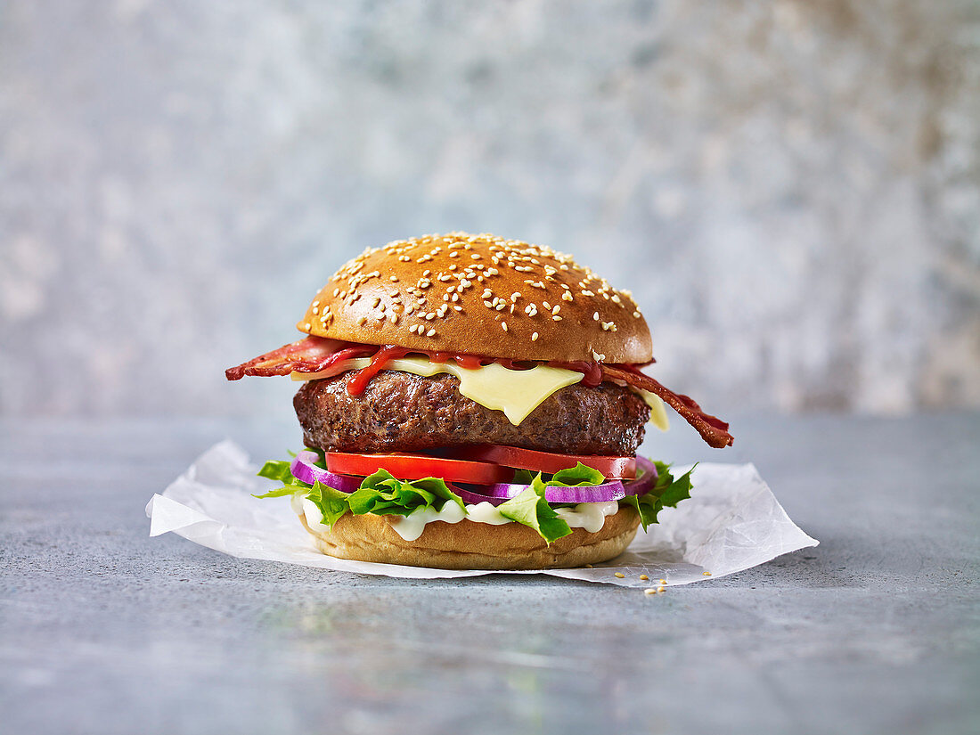 A beef burger with bacon against a light background in a sesame seed bun