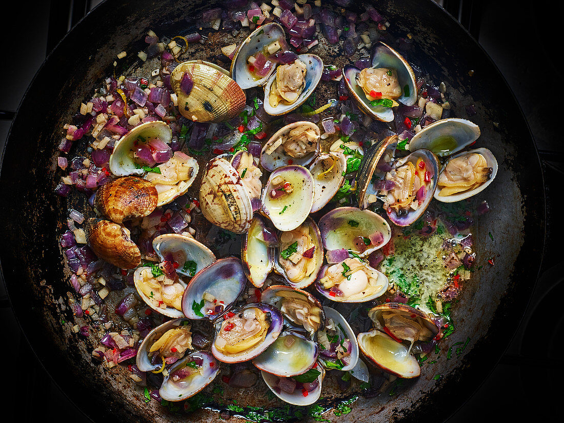 Clams cooking in apan with butter, chopped onions and garlic