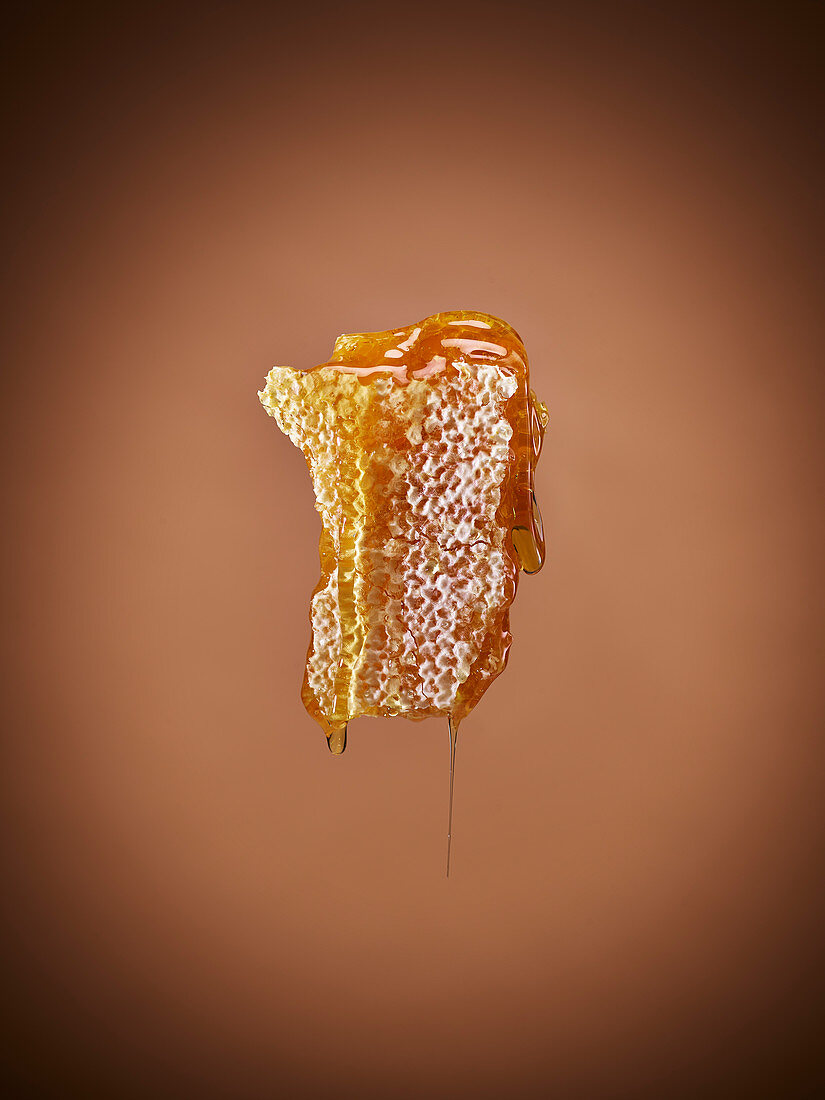 A honeycomb dripping with honey against an orange background