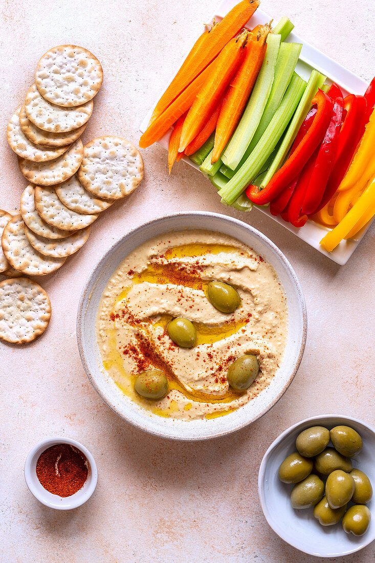 Hummus aus roten Linsen serviert mit Gemüsesticks, Crackern und Oliven