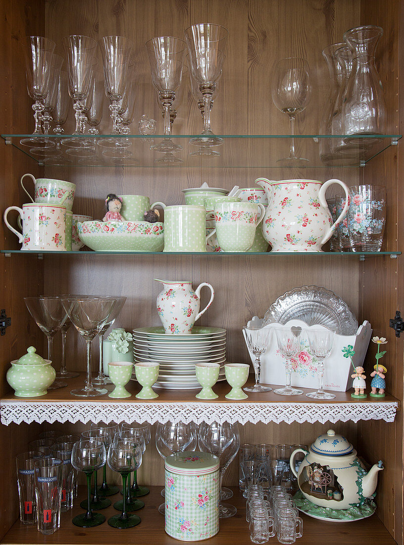 Glasses and vintage-style crockery in cupboard decorated with lace trim