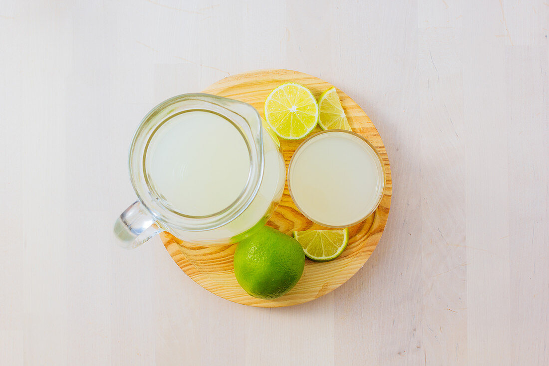 Homemade refreshing lemonade in server in glasses on wooden tray