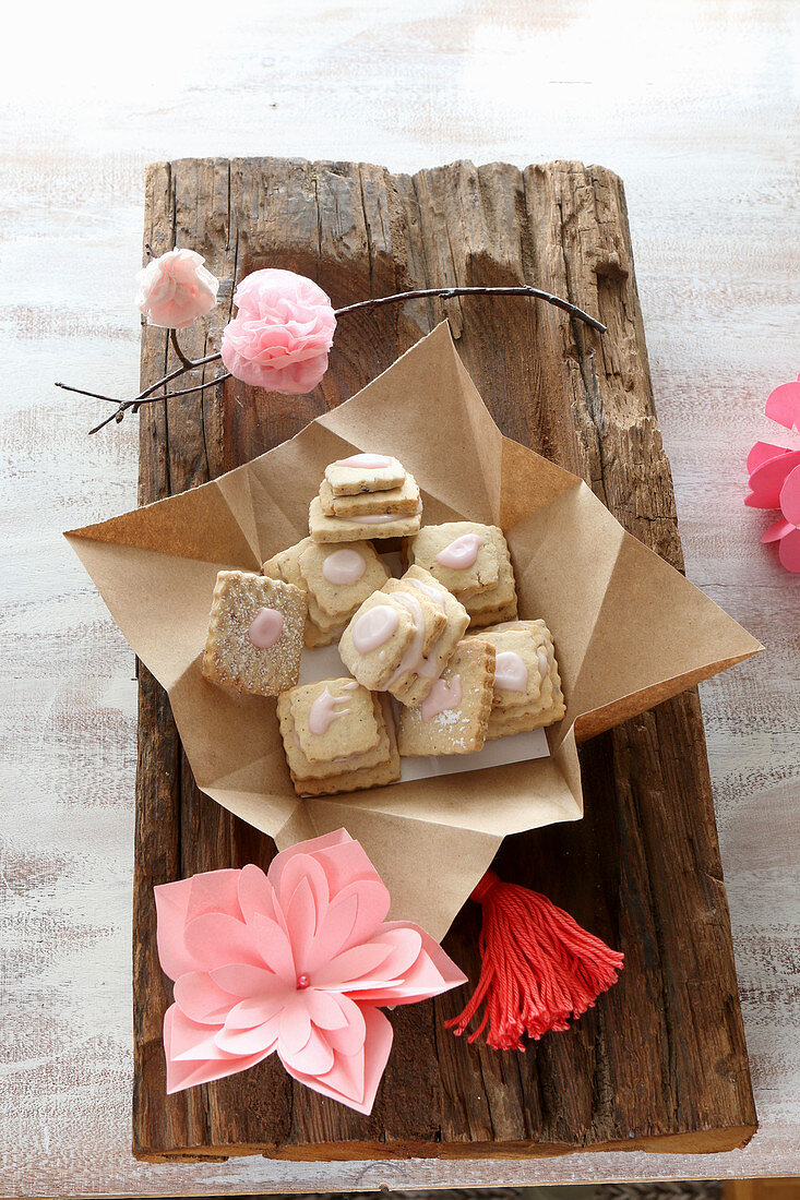 Glutenfreie Etagenkekse mit rosa Zuckerguss und rosa Papierblüten auf rustikalem Holzbrett