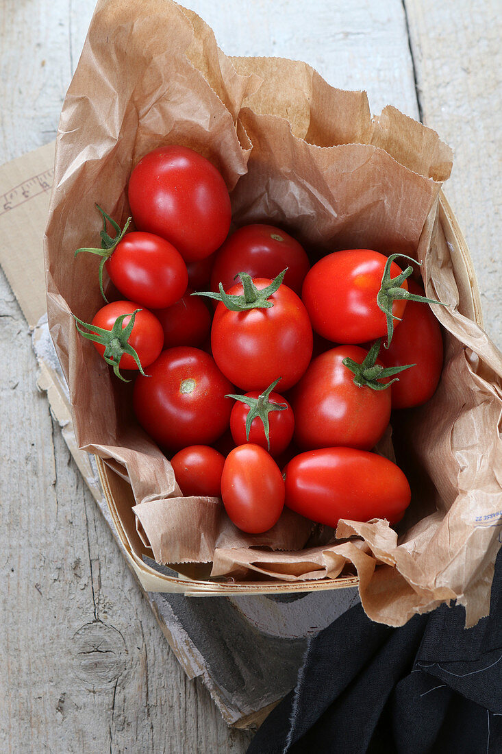 Fresh vine tomatoes in a paper bag in a wooden basket