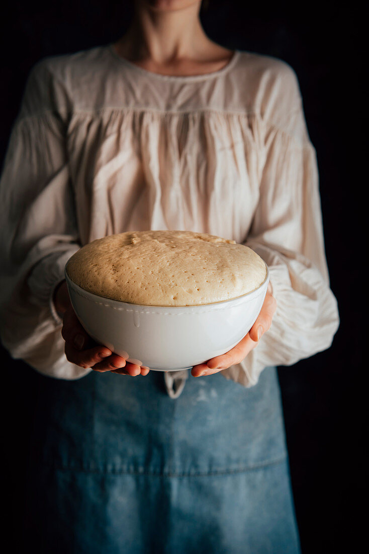 Woman holds a bowl of raised challah bread dough in her hands
