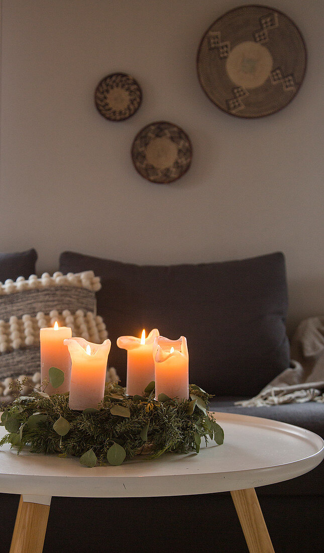 Adventskranz mit brennenden Kerzen im Wohnzimmer in Grau