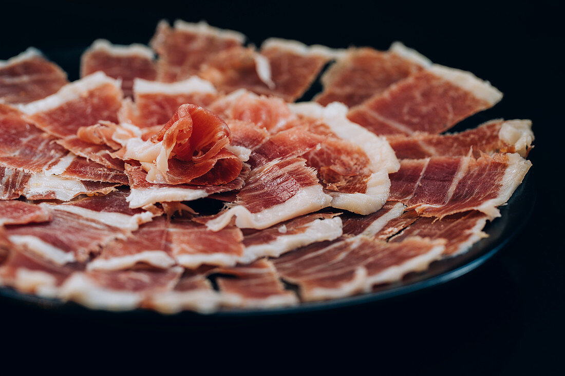 thin slices of ham with tallow lines served in plate on black background