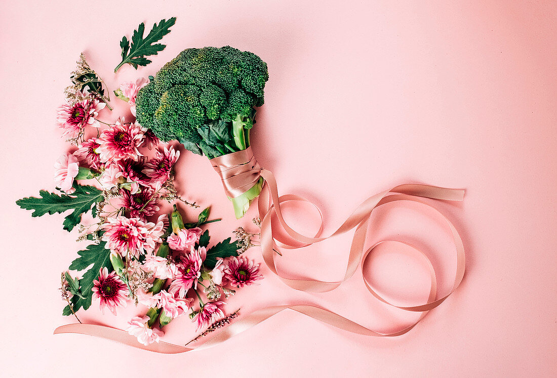 Bunch of pretty flowers and ripe broccoli with silk ribbon arranged on pink background