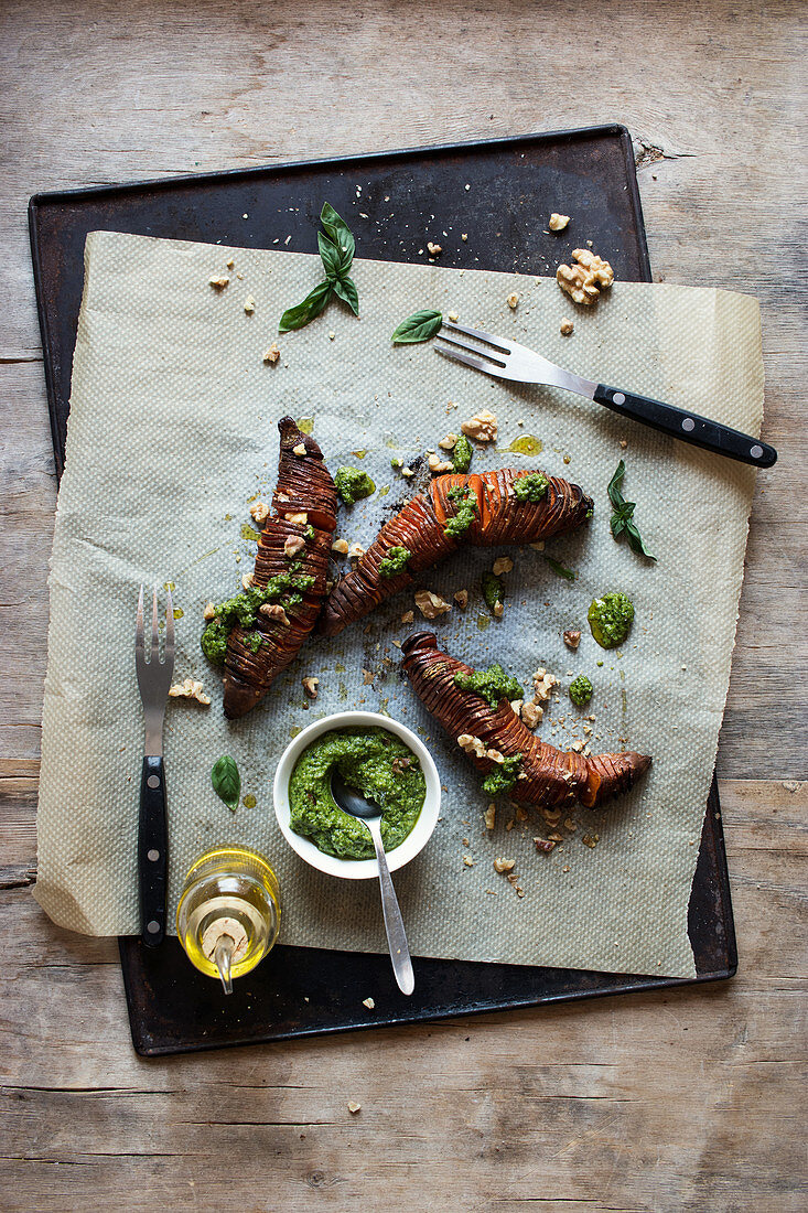 Sweet potato with fresh pesto sauce placed on tray and paper near forks and oil