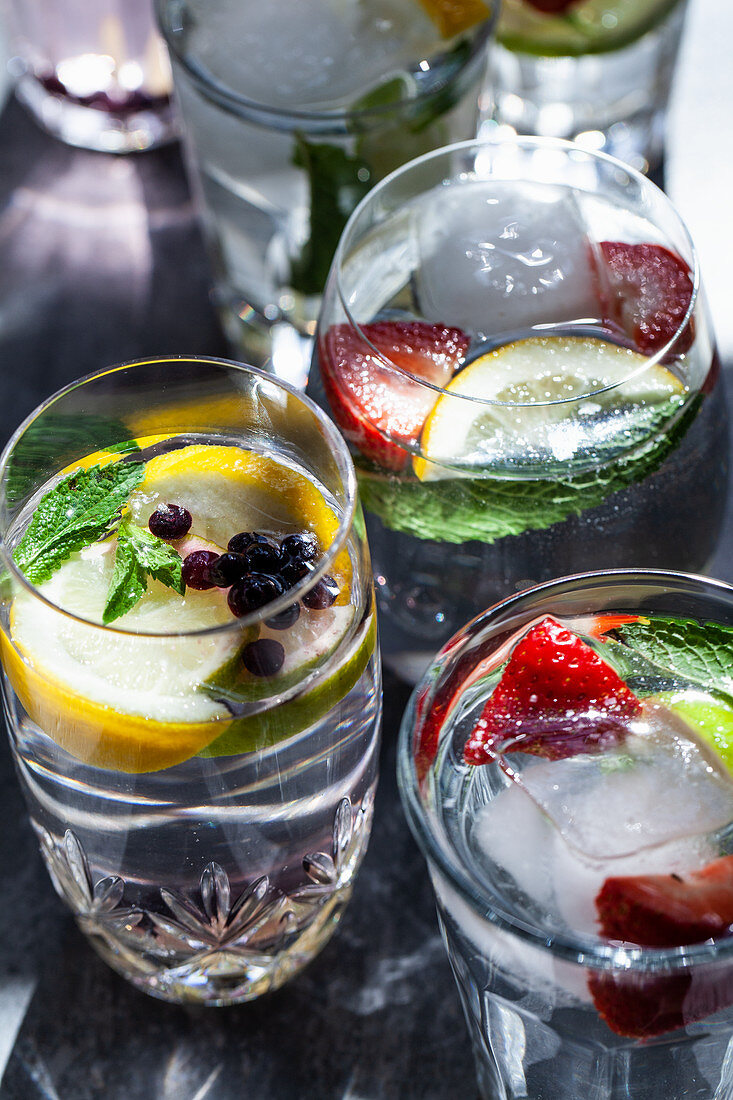 Various glasses of water filled with fruit, mint and ginger