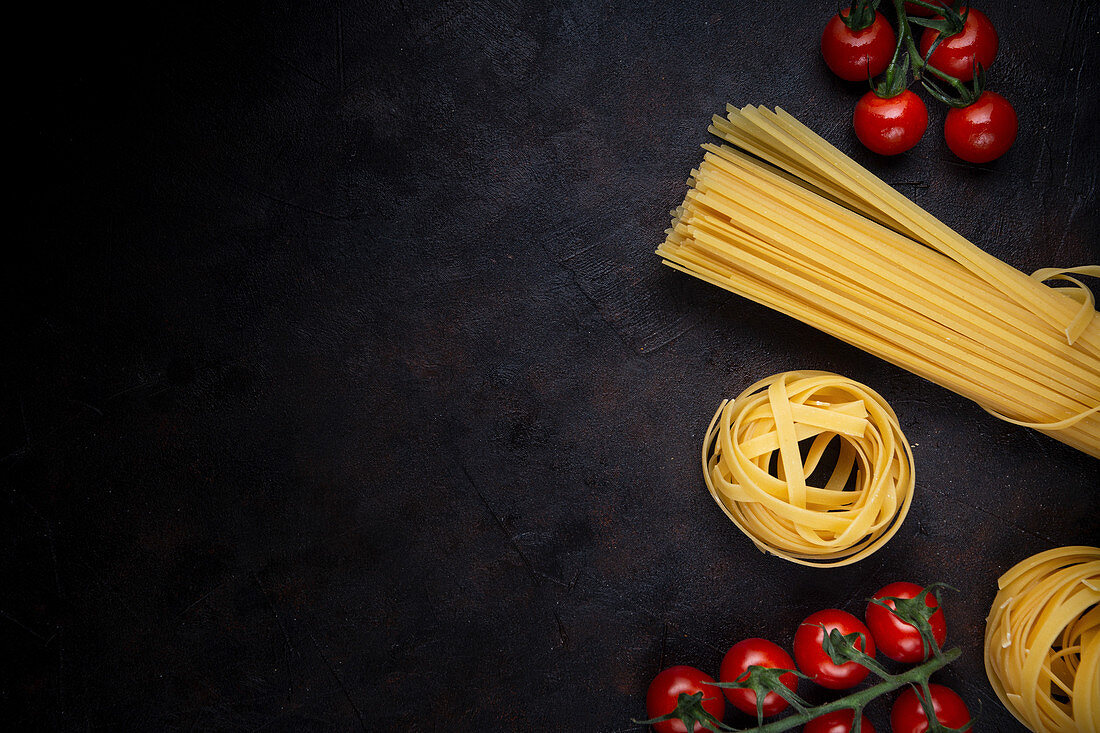 Bunch of uncooked pasta and ripe cherry tomatoes placed on black background