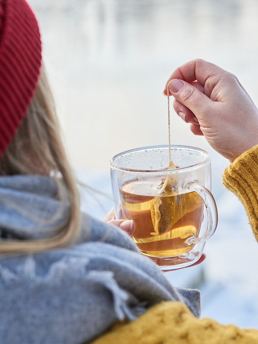 Frau in Winterkleidung hält eine Tasse Tee in der Hand