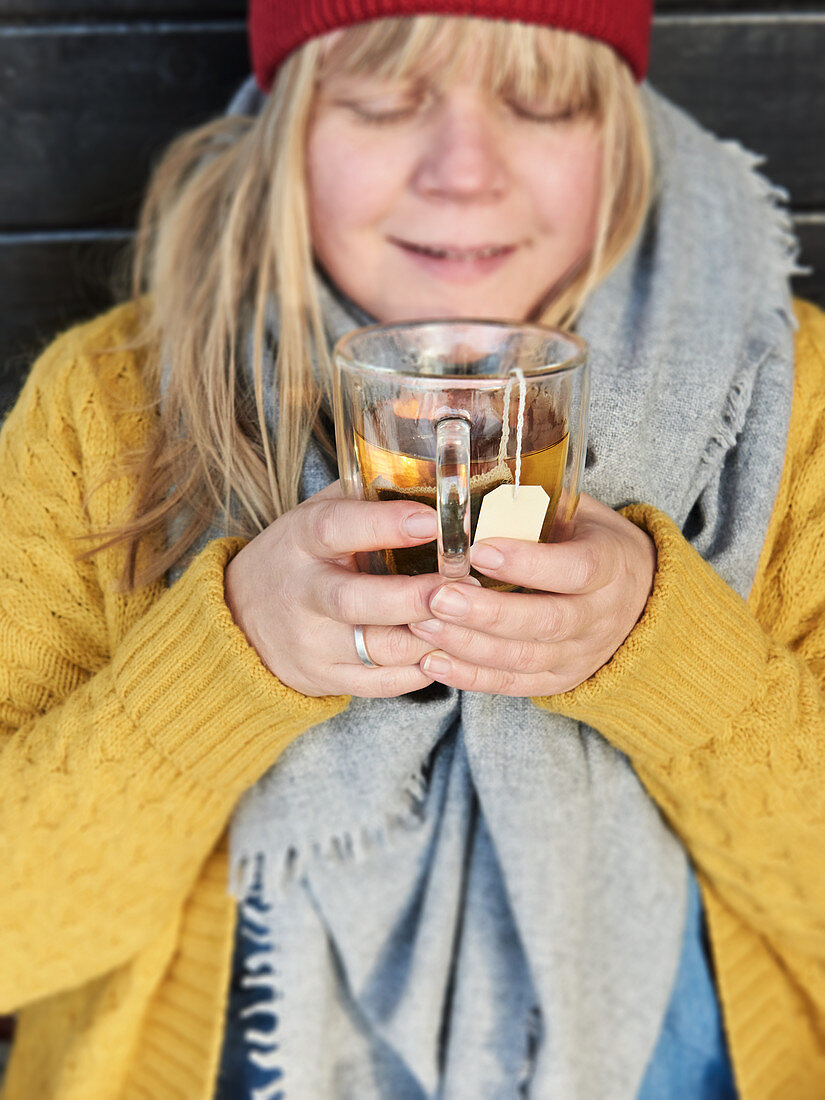 A woman wearing winter clothing holding a warm cup of tea