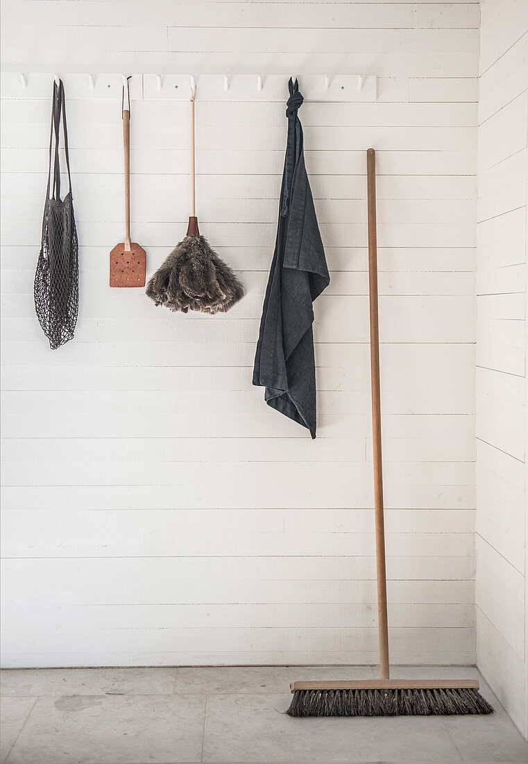 Cleaning utensils and dustpan hung from coat rack on white-painted wooden wall