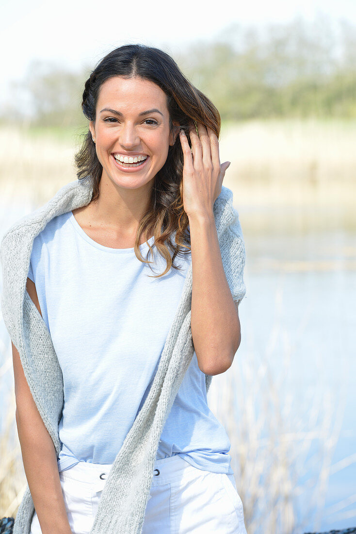 A young woman wearing a light-blue T-shirt with a jumper over her shoulders and white shorts near river