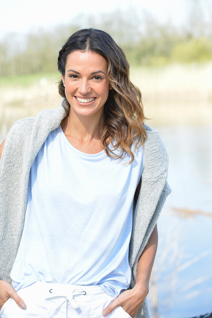 Junge Frau in hellblauem T-Shirt, Pulli über den Schultern und weißen Shorts am Fluss