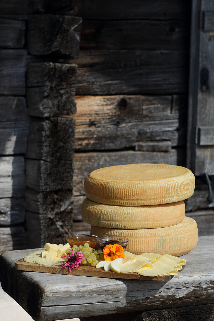 A supper board and cheese wheels on a wooden table outside an alpine hut
