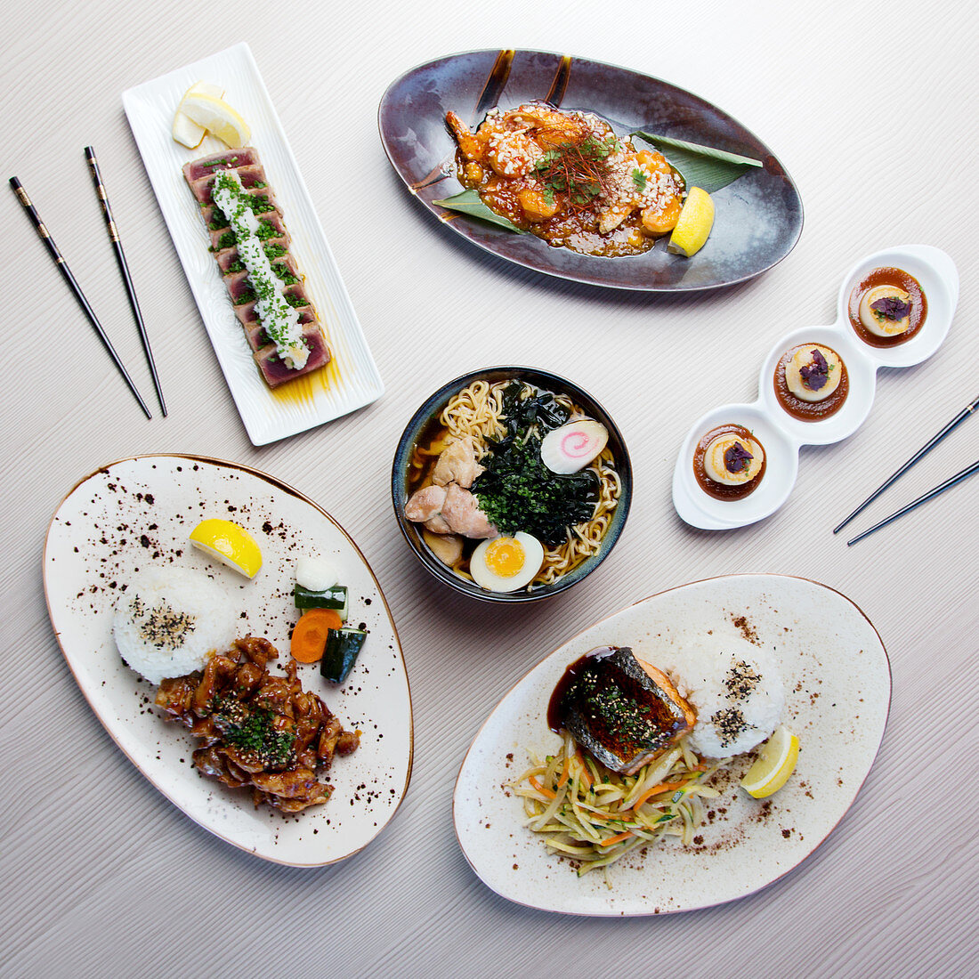 Japanese modern dishes on a table: Chicken Ramen, Tuna Tataki, Soba Chicken, Ebi Chilli Sauce, Grilled salmon and scallops with miso sauce