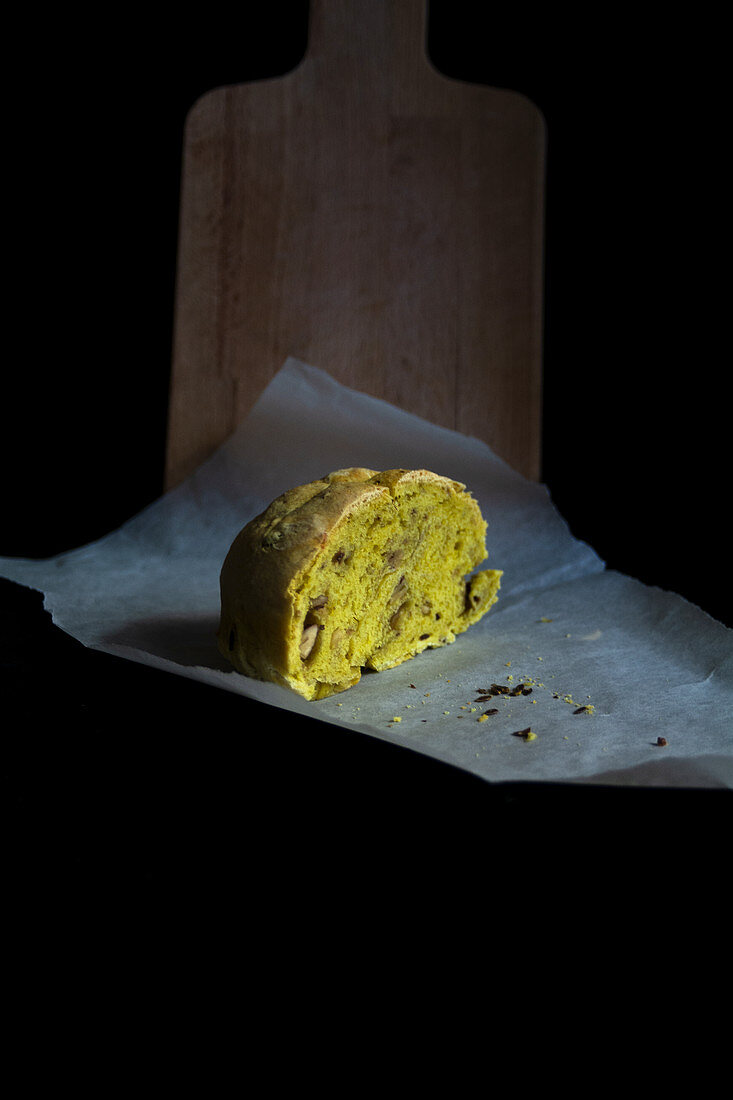 A piece of hand made bread with turmeric and walnuts on the black backdrop