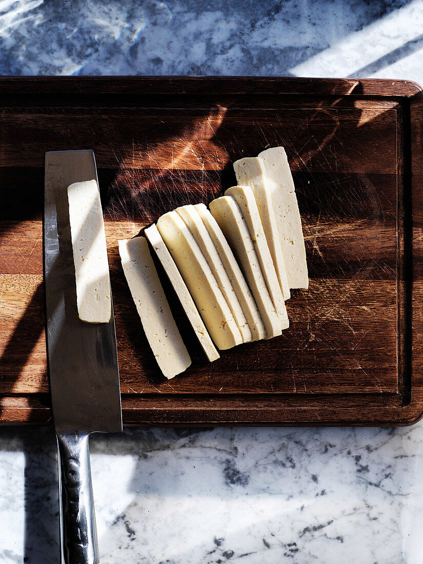 Slicing fresh pressed tofu on a dark wooden board