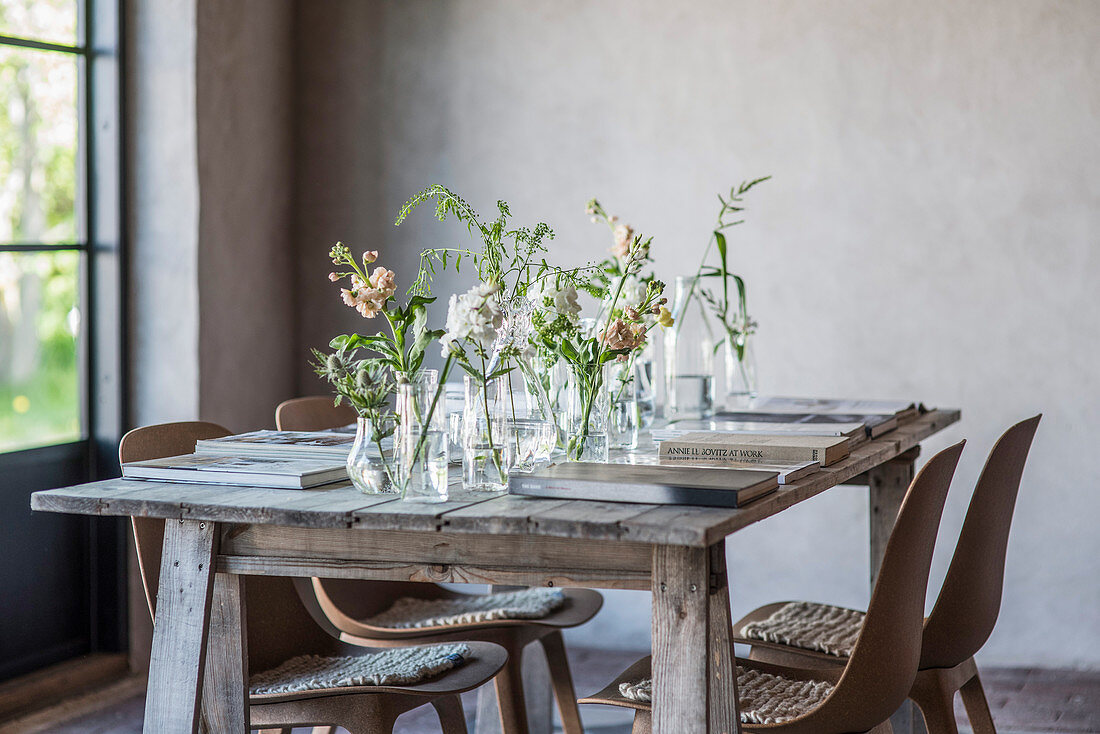 Flowers in various glass containers and books on rustic wooden table