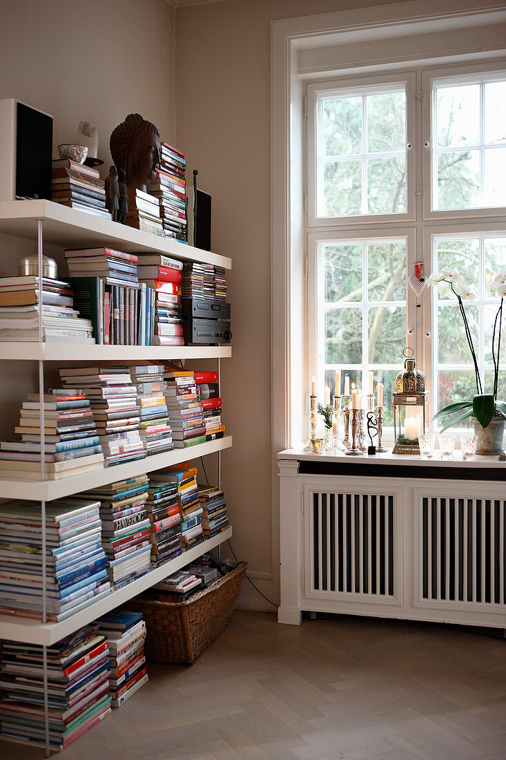 Books stacked on shelves next to window above radiator cover