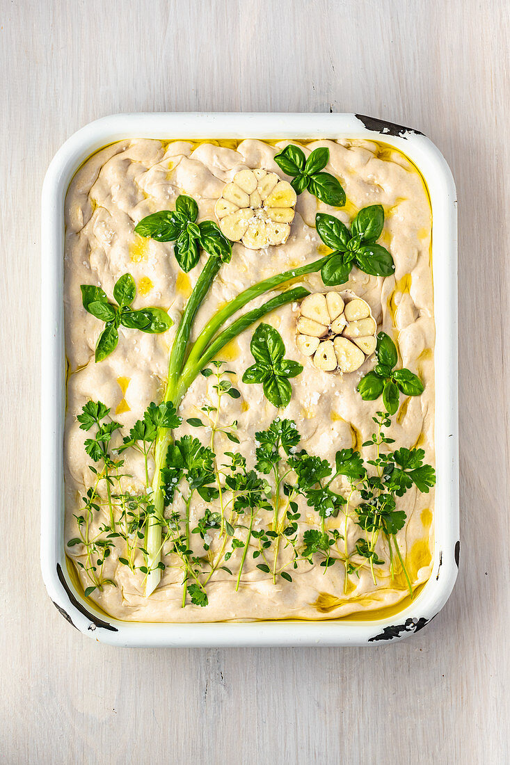 Ungebackenes Focaccia mit Blütenmotiv aus Kräutern, Lauchzwiebel und Knoblauch