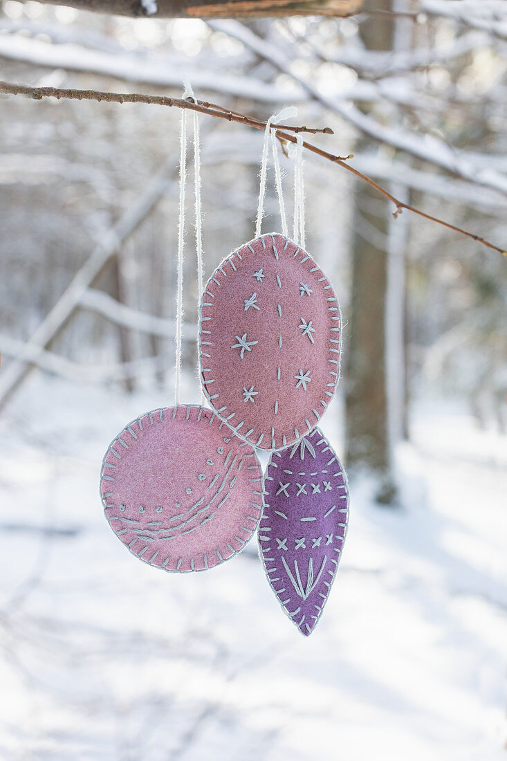 Handmade, embroidered felt decorations hung from branch in snowy garden
