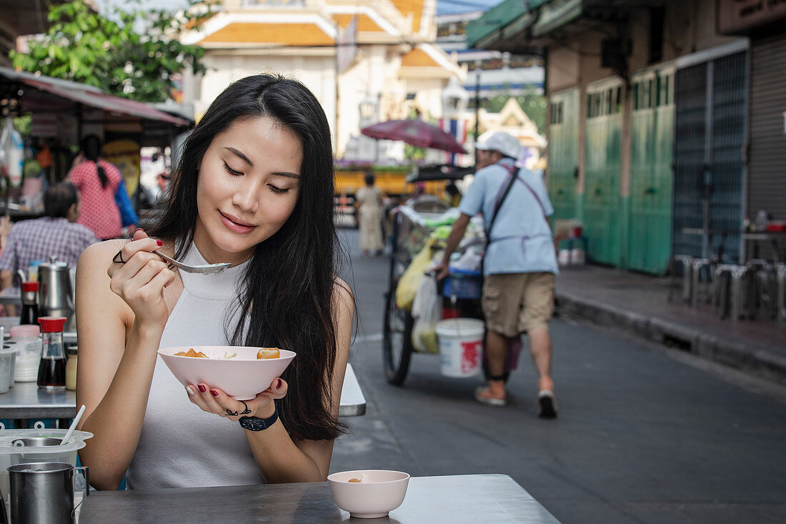 Junge Asiatin isst herzhaftes Congee (Reisporridge) zum Frühstück