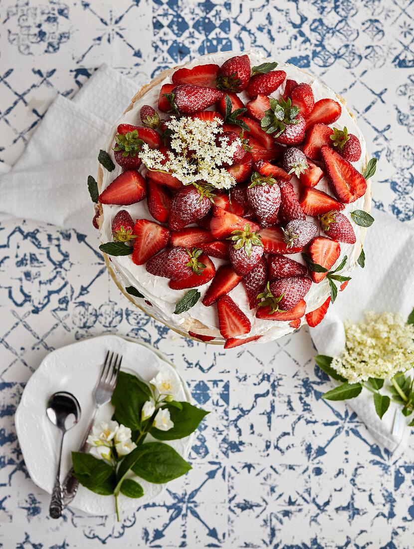 Pavlova cake with fresh strawberries garnished with fresh mint leaves and elderflower