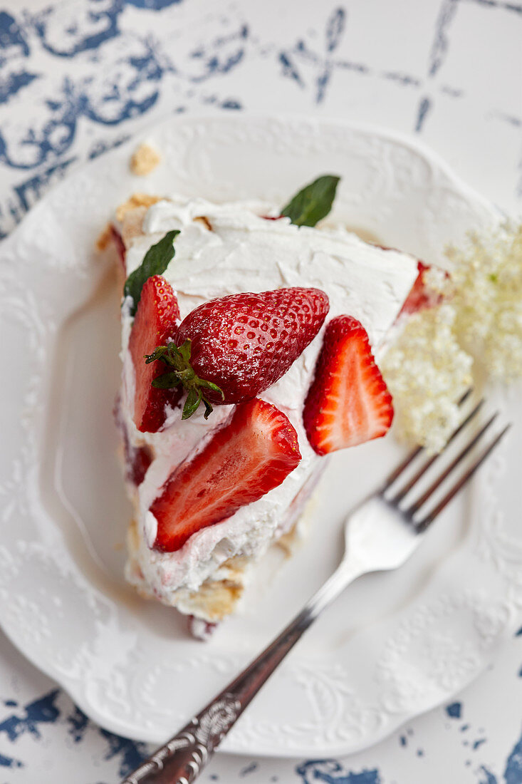Piece of Pavlova cake with fresh strawberries garnished with mint leaves and elderflower