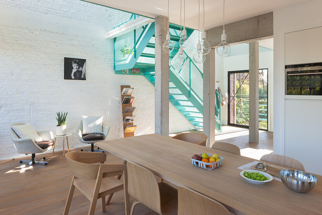 Helles Esszimmer mit Holztisch und weißer Backsteinwand, türkisfarbene Treppe im Hintergrund