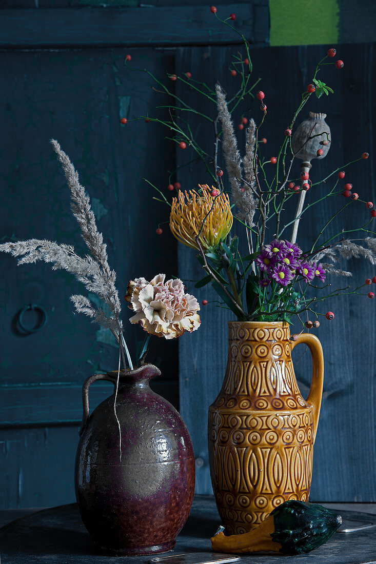 Herbststräuße mit Nelke, Nadelkissen, Chrysantheme, Hagebutten, Mohnkapsel und Gräserrispen in Vintage Krügen