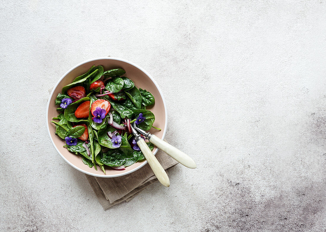 Fresh summer salad of spinach, strawberries, onions with balsamic vinegar and edible flowers
