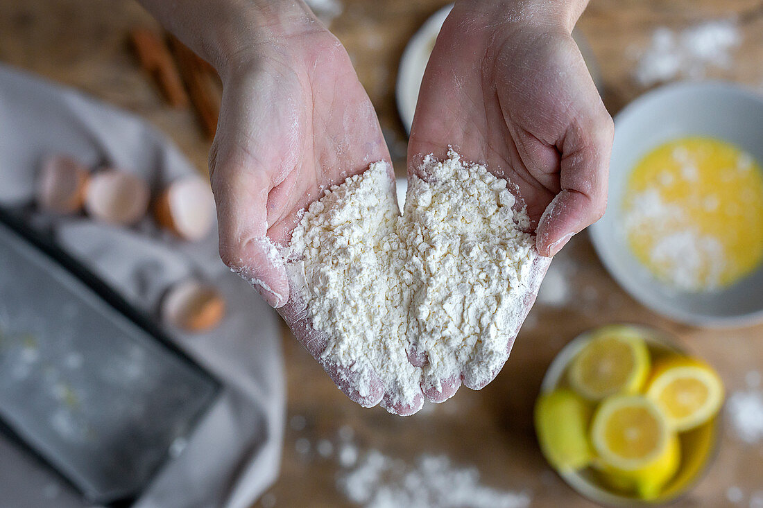Hands full of flour near black bowl while preparing pastry at home