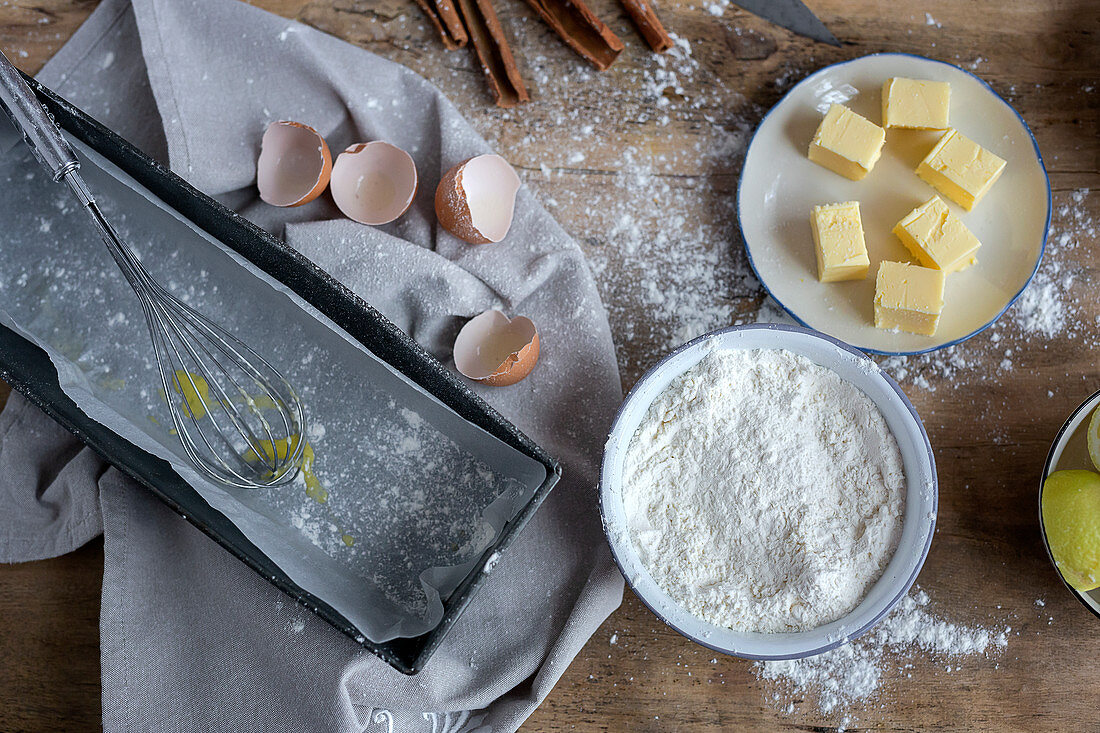 Ingredients for cake recipe including bowl with flour and egg placed on dusted wooden table