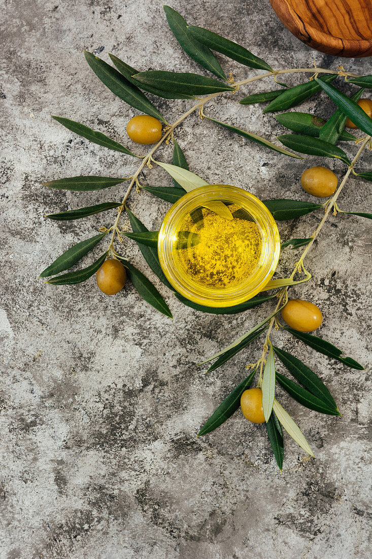 Bio-Olivenöl im Glas zwischen Olivenzweigen