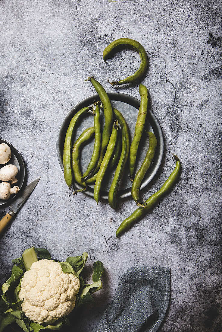 Organic green pods on round metal tray with mushrooms and cauliflower on grunge gray surface