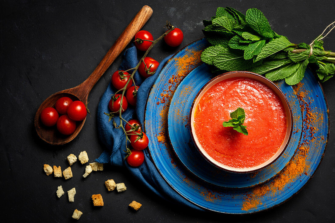 Healthy homemade tomato soup with bread, mint and olive oil on dark background