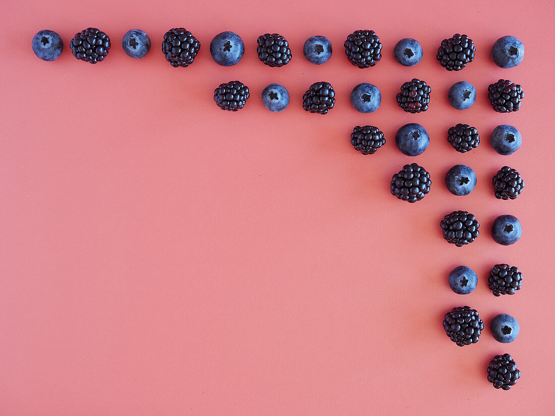 Creative natural background with fresh ripe blueberries and blackberries arranged in corner of pink surface