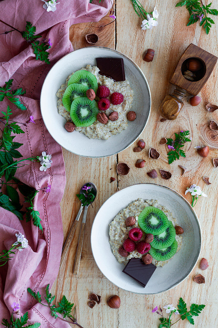 Slices of fresh kiwi and raspberries, chocolate and hazelnuts in bowl of healthy porridge