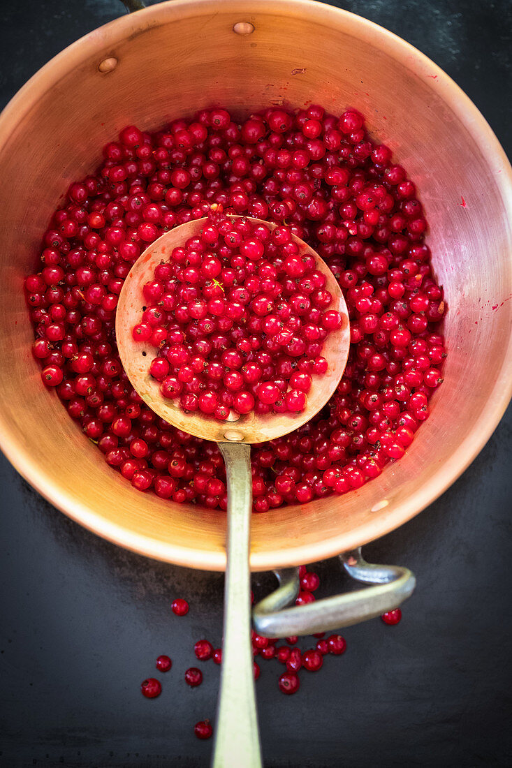 Rote Johannisbeeren zum Einkochen mit Sieblöffel in Kupfertopf