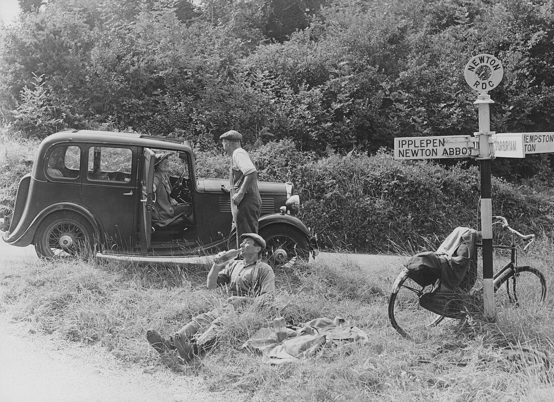 People relaxing by a signpost with a 1935 Standard, Devon