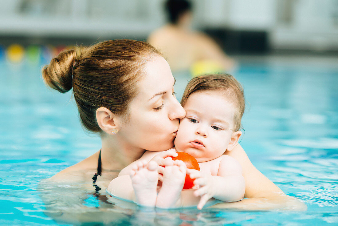 Mother kissing baby in swimming pool