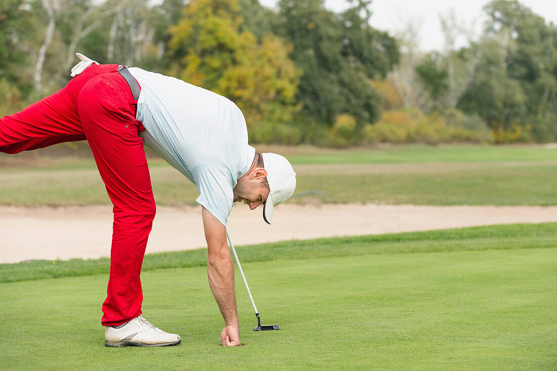 Golfer taking ball from hole