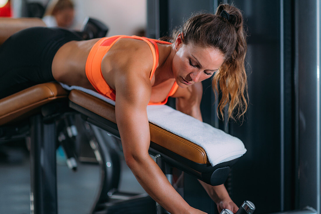 Female athlete using lying leg curl bench in the gym
