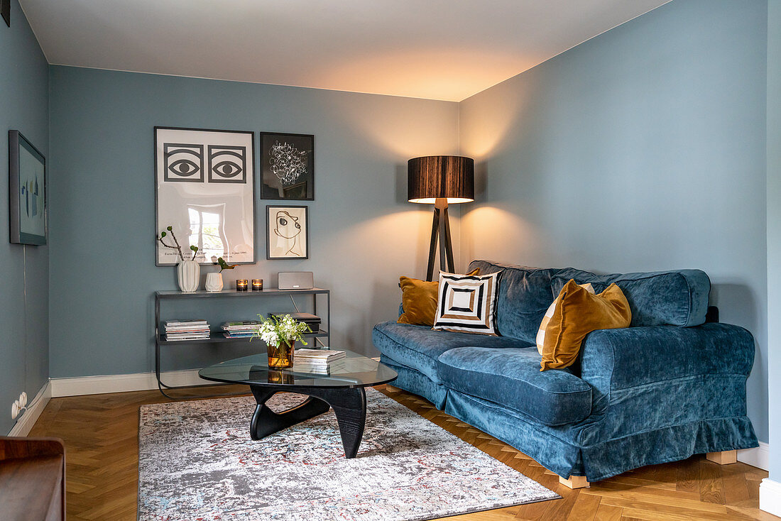 Blaues Sofa mit Samtbezug, Stehleuchte und Coffeetable im Zimmer mit blauen Wänden