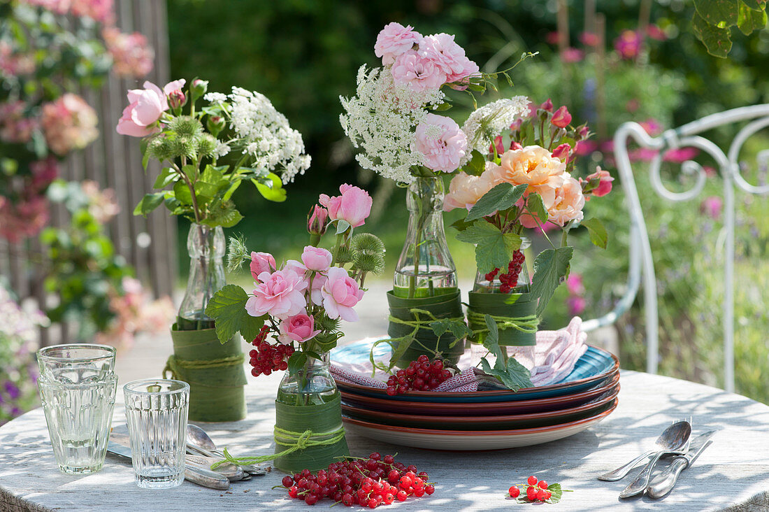 Small bouquets of rose petals and large Burnet saxifrage in bottles as table decorations, red currants