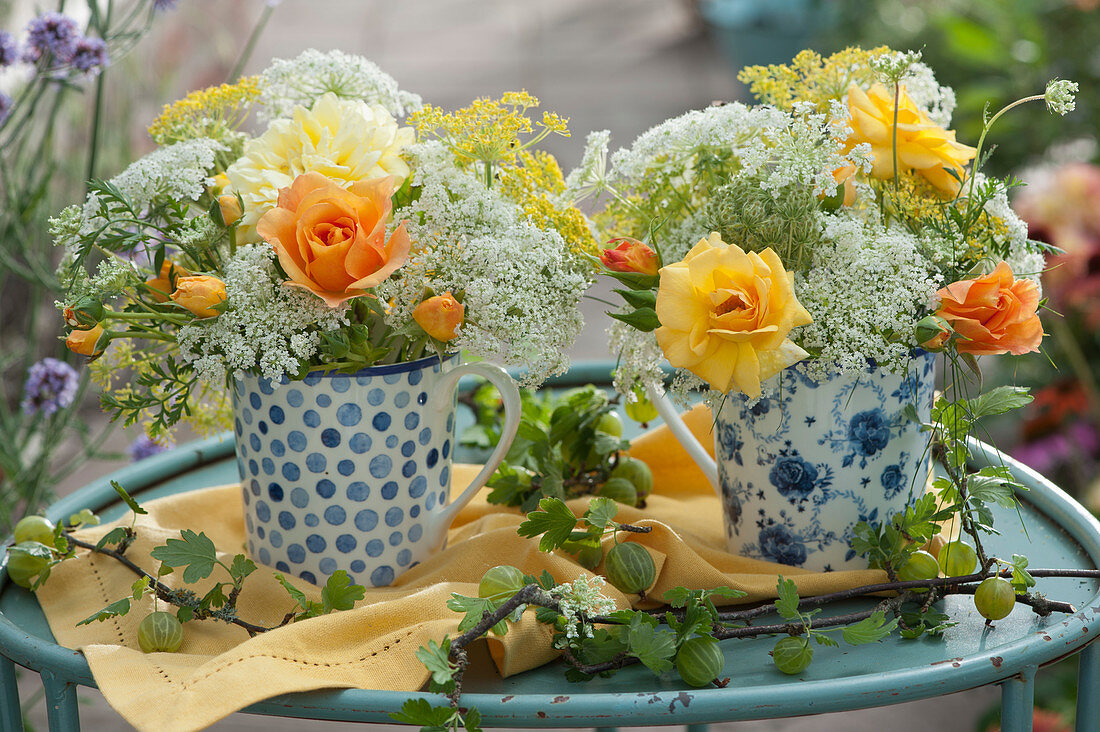 Small bouquets of roses, wild carrot, fennel and cumin in coffee cups, branches with gooseberries as decoration